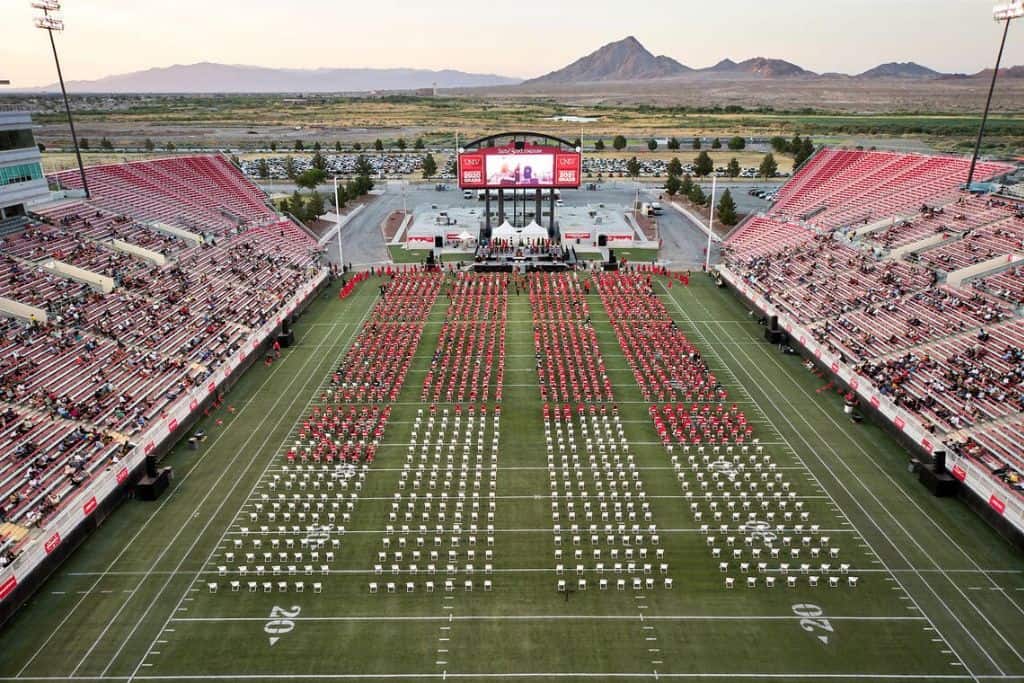 overview outdoor commencement in football stadium with graduates dressed in red regalia on the field